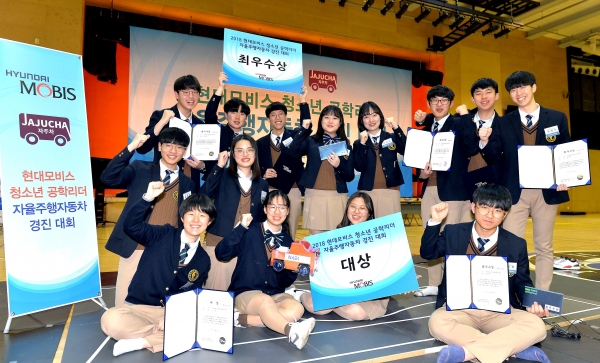 인천 하늘고등학교에서 개최된 ‘현대모비스 청소년 공학리더 자율주행차 경진대회’에 참가한 아이들이 모형 도로 앞에서 손을 들어 보이고 있다 [사진=현대모비스]