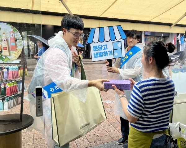 동서발전 직원들이 명동 일대 상가에 방문해 문닫고 냉방하기 참여를 부탁하면서 손선풍기를 전달하고 있는 모습 [사진=동서발전]