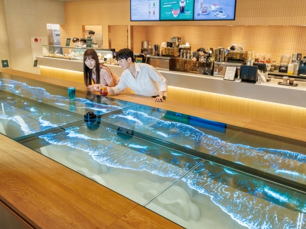 LG디스플레이 모델이 스타벅스 '더여수돌산DT점'에서 55인치 투명 OLED 12대를 이어붙인 초대형 투명 OLED 테이블을 체험하고 있다. [사진=LG디스플레이]